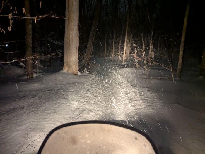 Headlight on the trail during a night ride in falling snow